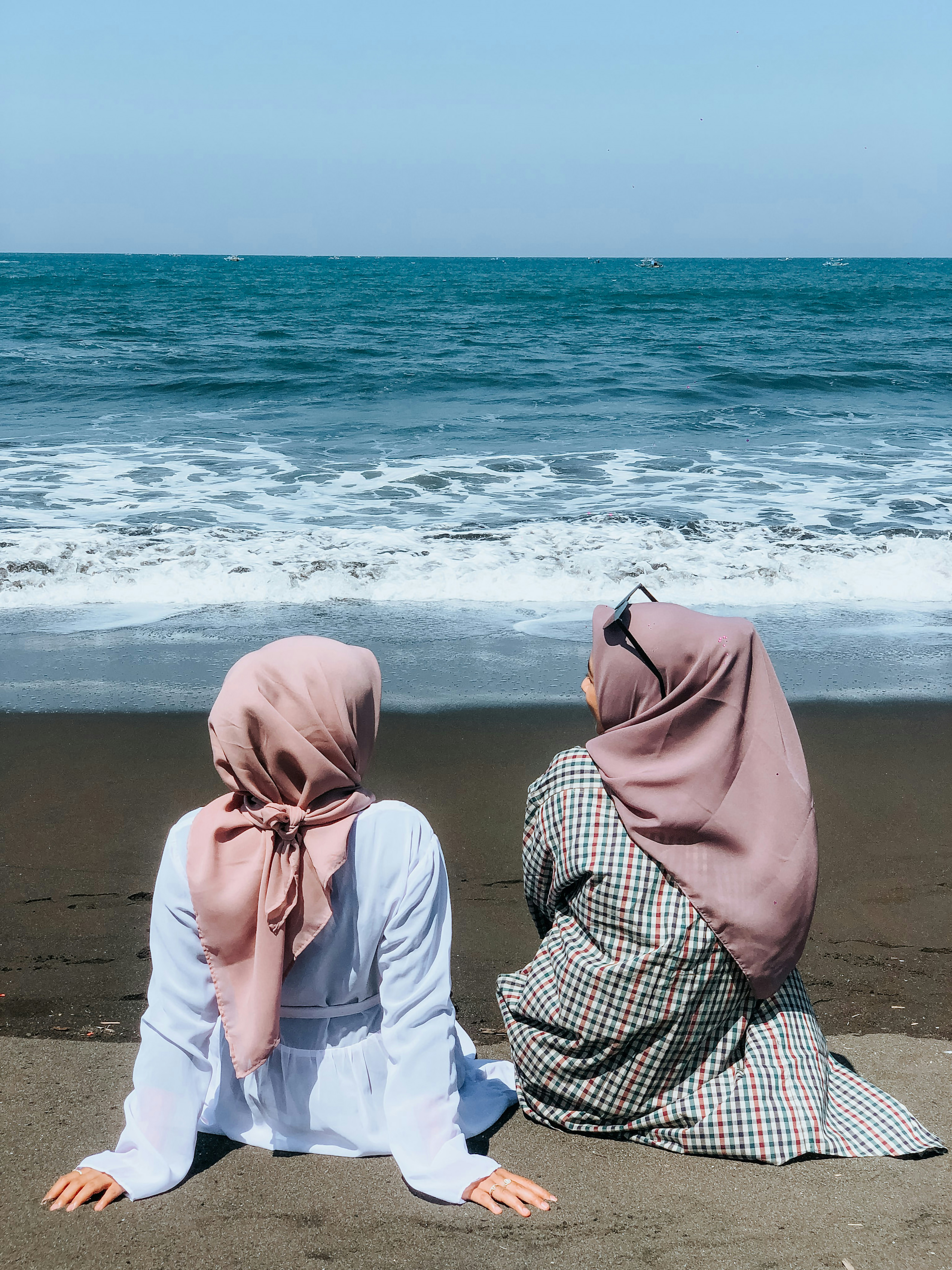 Two women sitting on a beach facing the ocean